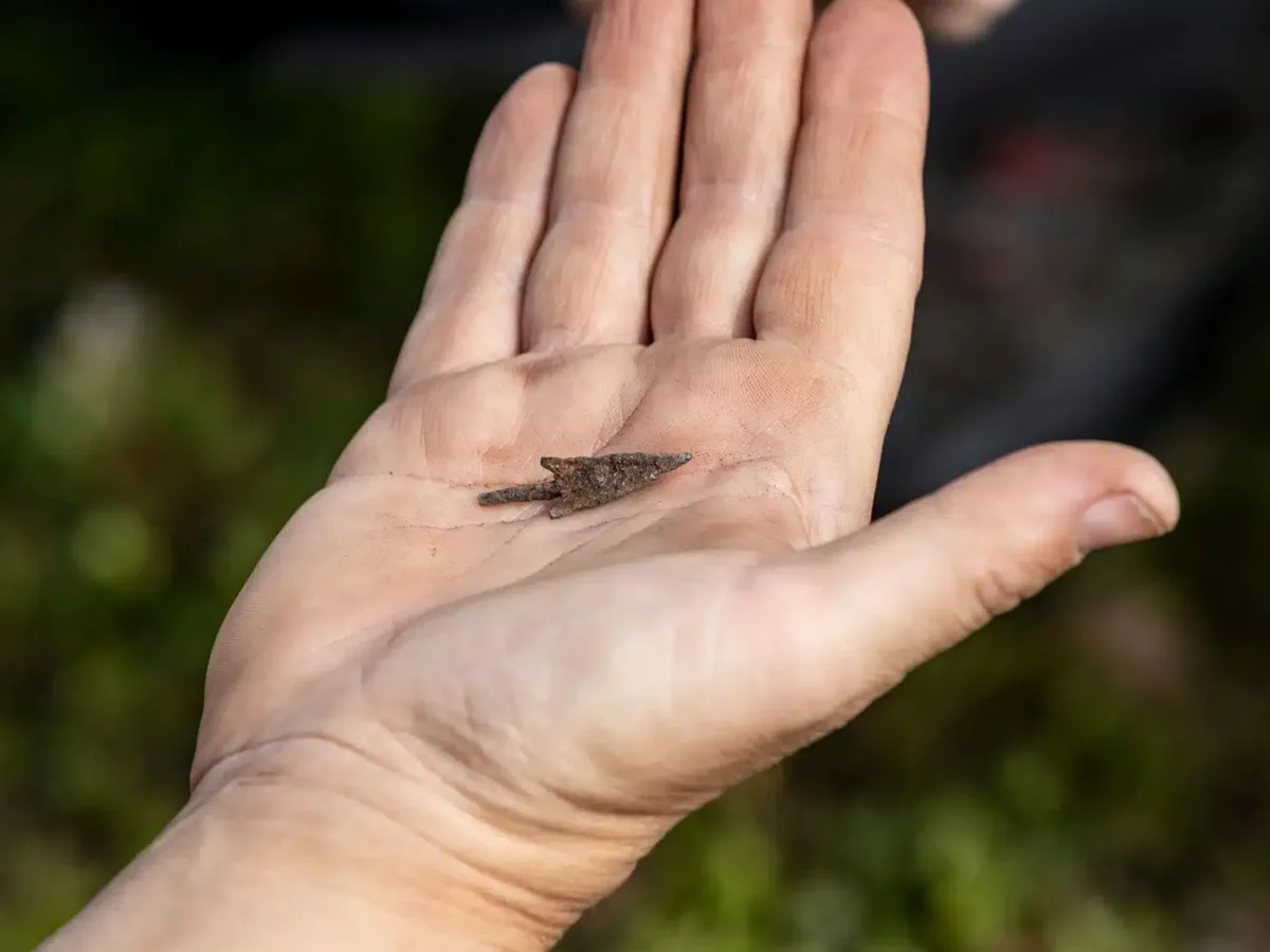 Un vârf de săgeată mic și ruginit zace în palma unei mâini