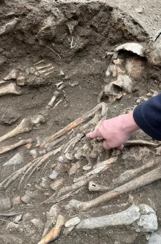 Arheologul Walter Pantano arată cu degetul spre cuiul care se află pe pieptul unuia dintre schelete, la noul sit de săpături