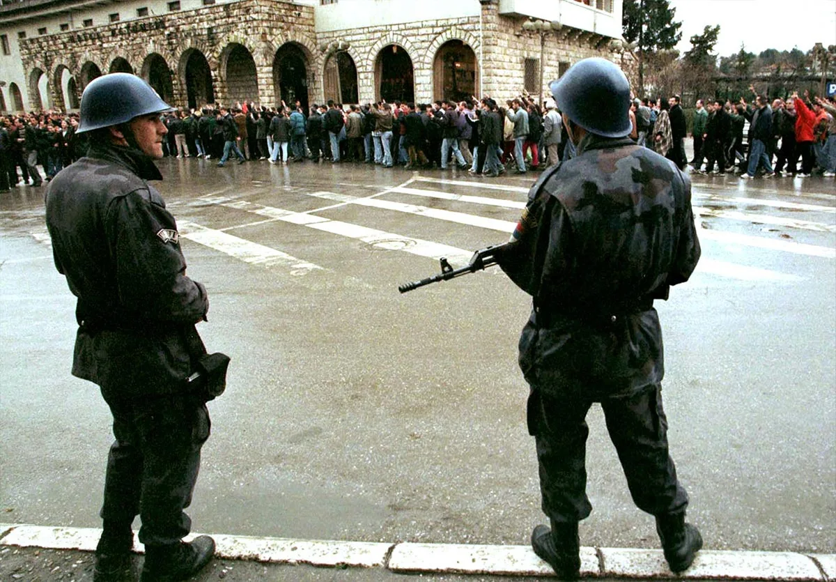 Polițiști sârbi supraveghează cetățeni de etnie albaneză în timpul unei manifestații în Pec, astăzi Peje, în 1998